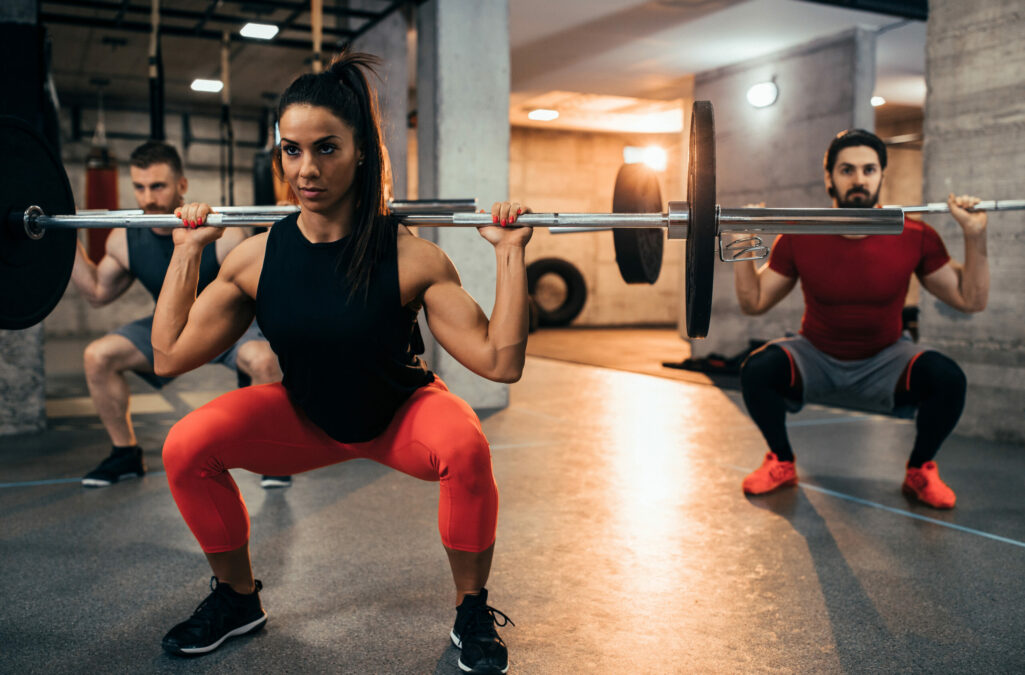Shot of two young men and a woman lifting weights at the gym